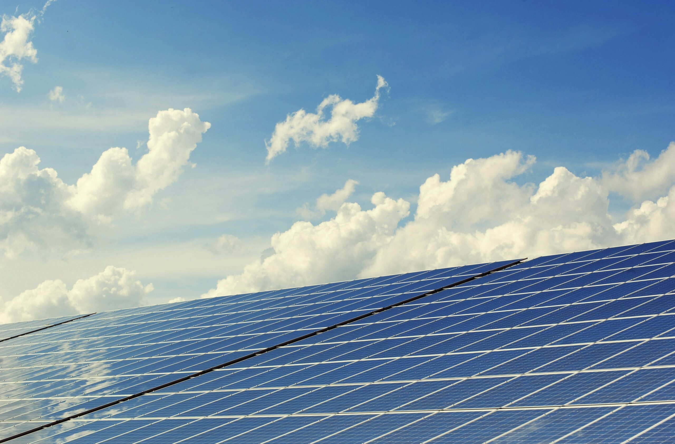 Solar panels leaning under a blue sky with white clouds.