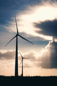 Two wind turbines silhouetted against a cloudy sky in the twilight.